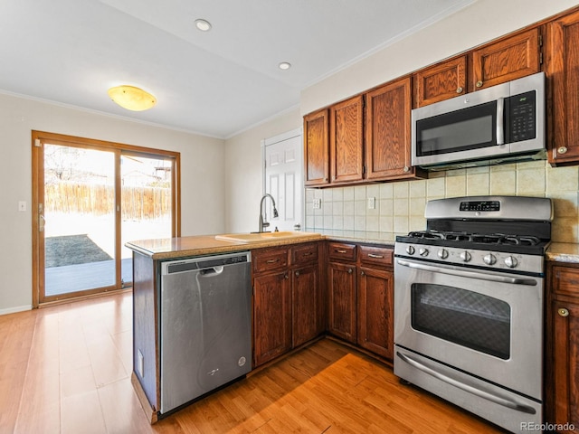 kitchen with sink, ornamental molding, appliances with stainless steel finishes, kitchen peninsula, and backsplash