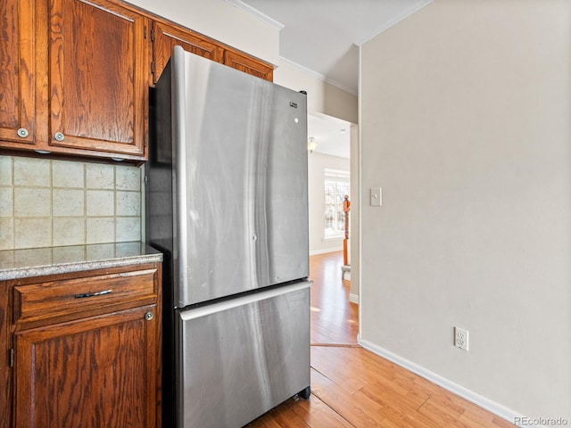 kitchen featuring tasteful backsplash, crown molding, light hardwood / wood-style flooring, and stainless steel refrigerator