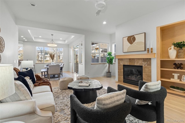 living room featuring recessed lighting, a raised ceiling, wood finished floors, a tile fireplace, and baseboards