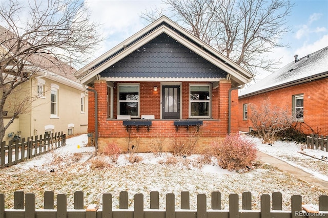 bungalow-style house featuring covered porch, brick siding, and a fenced front yard