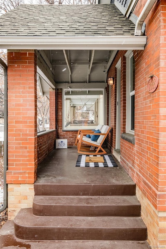 exterior space featuring a shingled roof, covered porch, and brick siding