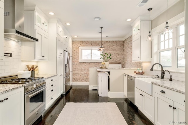 kitchen featuring visible vents, wall chimney exhaust hood, appliances with stainless steel finishes, white cabinetry, and a sink