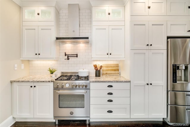 kitchen featuring stainless steel appliances, white cabinetry, glass insert cabinets, and wall chimney range hood