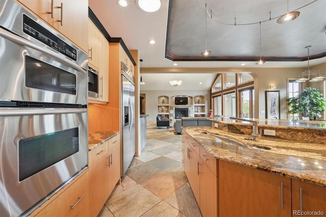 kitchen with decorative light fixtures, stainless steel appliances, stone counters, and a tray ceiling