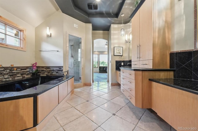 kitchen with hanging light fixtures, light brown cabinetry, ceiling fan, and dark stone countertops