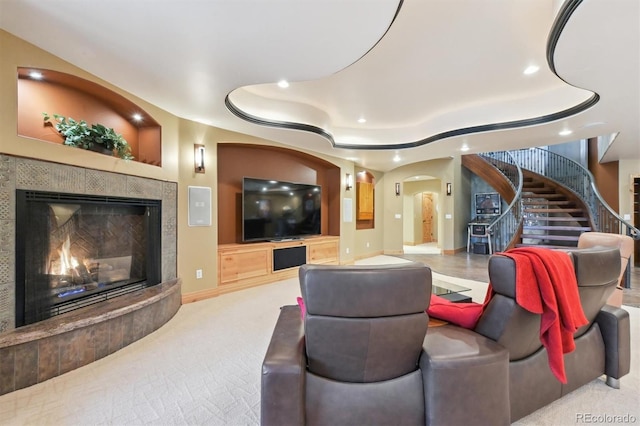 living room featuring a tile fireplace, built in shelves, light carpet, and a raised ceiling