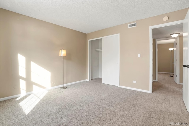 unfurnished bedroom featuring a textured ceiling, light carpet, and a closet