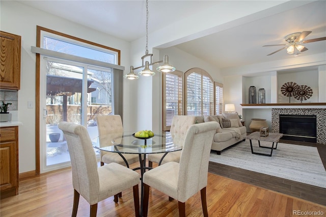 dining space featuring a tile fireplace, light hardwood / wood-style floors, plenty of natural light, and ceiling fan