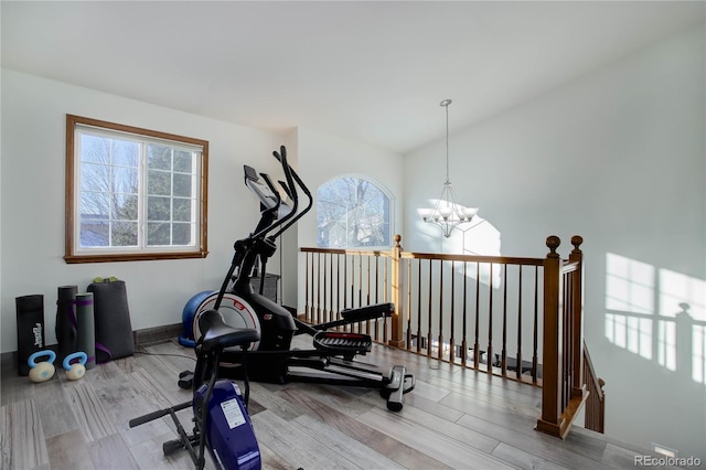 workout area featuring wood-type flooring, lofted ceiling, a wealth of natural light, and a notable chandelier