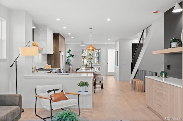 kitchen featuring sink, a kitchen bar, light wood-type flooring, backsplash, and hanging light fixtures