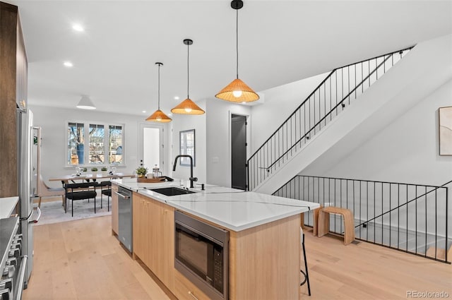 kitchen with sink, light wood-type flooring, a kitchen island with sink, and appliances with stainless steel finishes