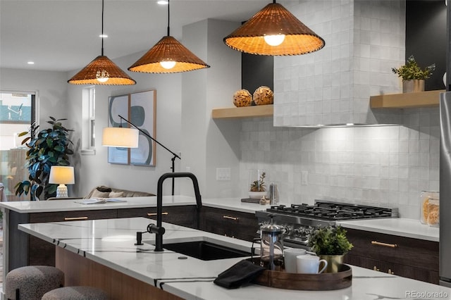 kitchen with sink, stainless steel gas cooktop, tasteful backsplash, dark brown cabinetry, and pendant lighting