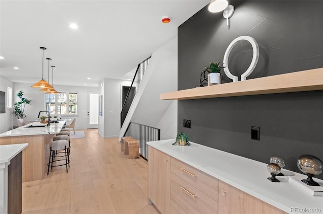 kitchen with hanging light fixtures, an island with sink, light brown cabinetry, a breakfast bar, and sink