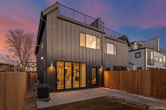 back house at dusk with central AC and a patio area