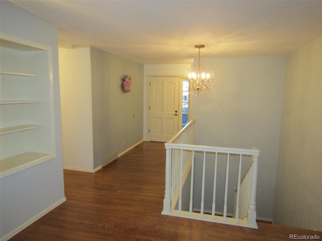 hallway with dark wood-type flooring and an inviting chandelier