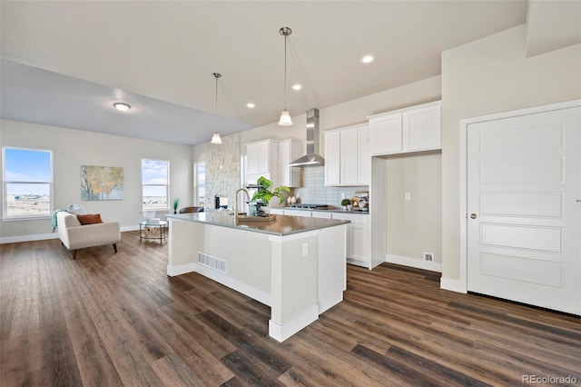 kitchen featuring wall chimney range hood, tasteful backsplash, visible vents, and white cabinets