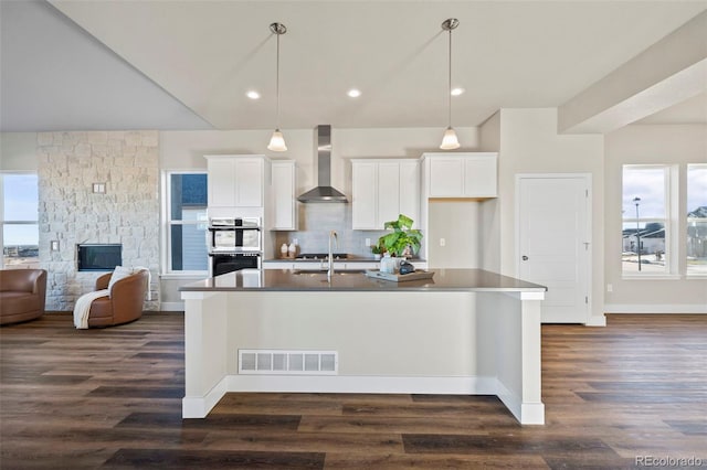 kitchen featuring a center island with sink, visible vents, wall chimney range hood, a fireplace, and a sink