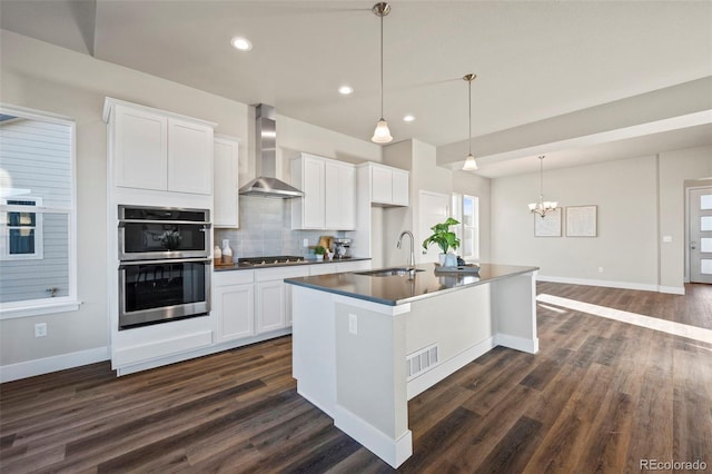 kitchen with tasteful backsplash, wall chimney exhaust hood, appliances with stainless steel finishes, white cabinetry, and a sink