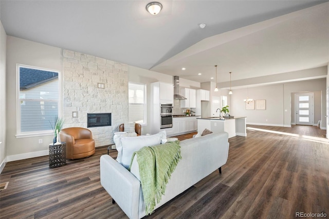 living room with visible vents, dark wood-type flooring, vaulted ceiling, a stone fireplace, and baseboards