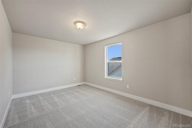 unfurnished room with light carpet, baseboards, and a textured ceiling