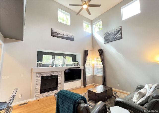 living room featuring ceiling fan, light hardwood / wood-style floors, a stone fireplace, and a towering ceiling