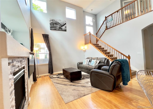 living room with a stone fireplace, a chandelier, a towering ceiling, and light hardwood / wood-style floors