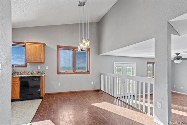 kitchen with sink, vaulted ceiling, black dishwasher, pendant lighting, and light hardwood / wood-style floors