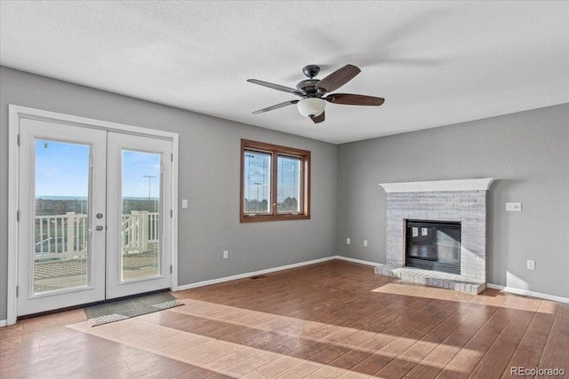 unfurnished living room featuring a brick fireplace, a healthy amount of sunlight, hardwood / wood-style floors, and french doors