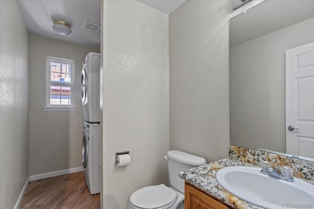 bathroom with hardwood / wood-style flooring, stacked washer and dryer, vanity, and toilet