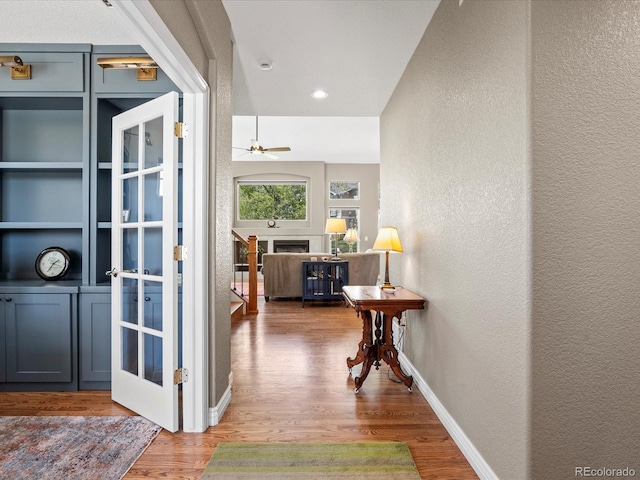 hall with a textured wall, wood finished floors, and baseboards