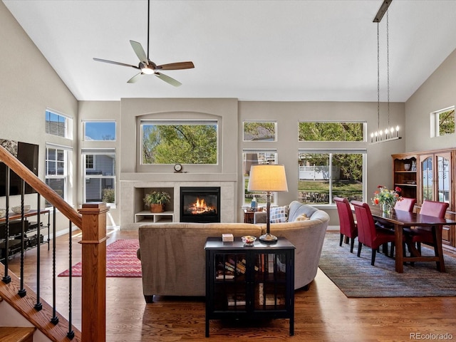 living room with ceiling fan, high vaulted ceiling, a fireplace, wood finished floors, and stairs