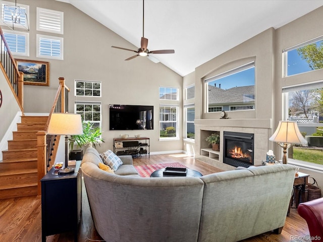 living area with wood finished floors, high vaulted ceiling, stairway, a tiled fireplace, and ceiling fan