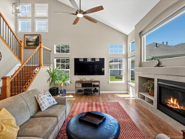 living area with wood finished floors, high vaulted ceiling, stairway, a ceiling fan, and a tiled fireplace