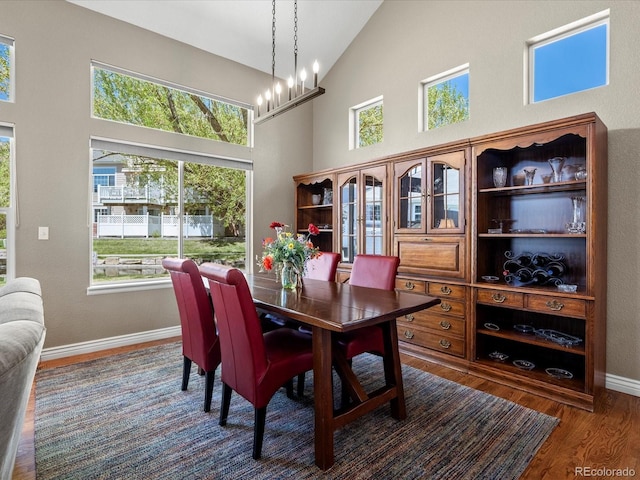 dining room featuring dark wood-type flooring, baseboards, high vaulted ceiling, and a chandelier