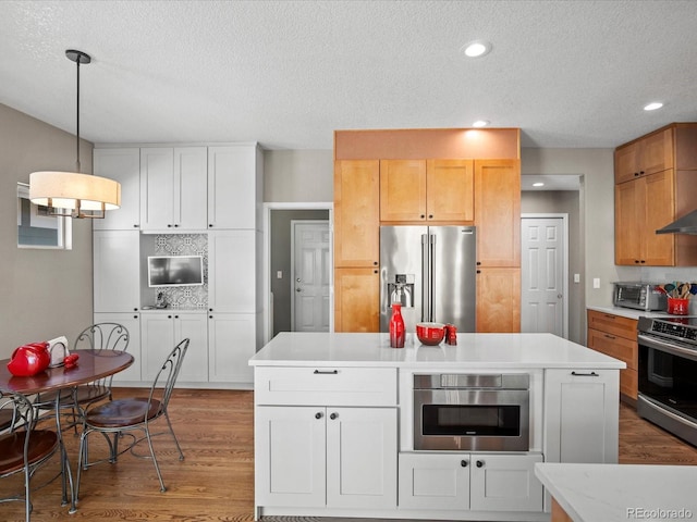 kitchen with appliances with stainless steel finishes, a textured ceiling, wood finished floors, light countertops, and a kitchen island