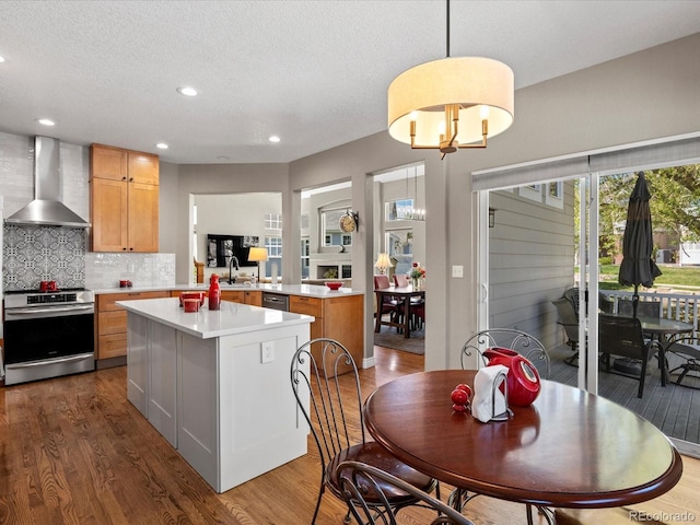 kitchen with wall chimney range hood, appliances with stainless steel finishes, light countertops, a center island, and dark wood finished floors