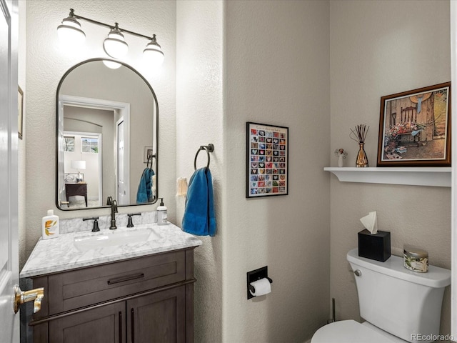 bathroom with toilet, vanity, and a textured wall