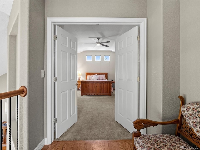 corridor with lofted ceiling, carpet floors, and a textured wall
