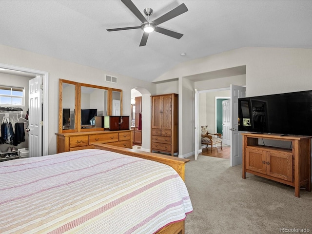 bedroom featuring lofted ceiling, light carpet, arched walkways, a spacious closet, and a ceiling fan