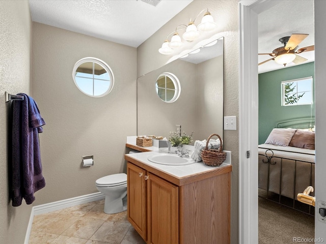 bathroom featuring baseboards, vanity, a textured wall, toilet, and ceiling fan