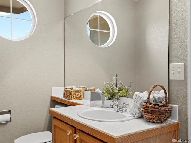 bathroom featuring toilet, a textured wall, and vanity