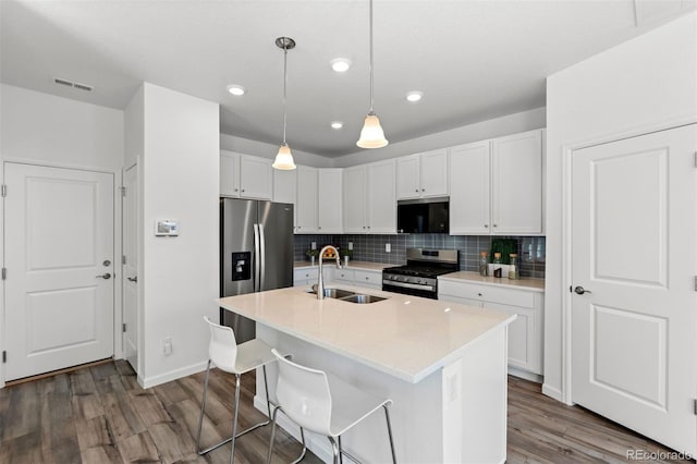 kitchen with a kitchen island with sink, stainless steel appliances, a sink, white cabinetry, and hanging light fixtures