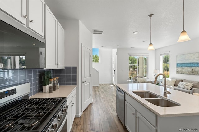 kitchen featuring a center island with sink, stainless steel appliances, light countertops, open floor plan, and a sink