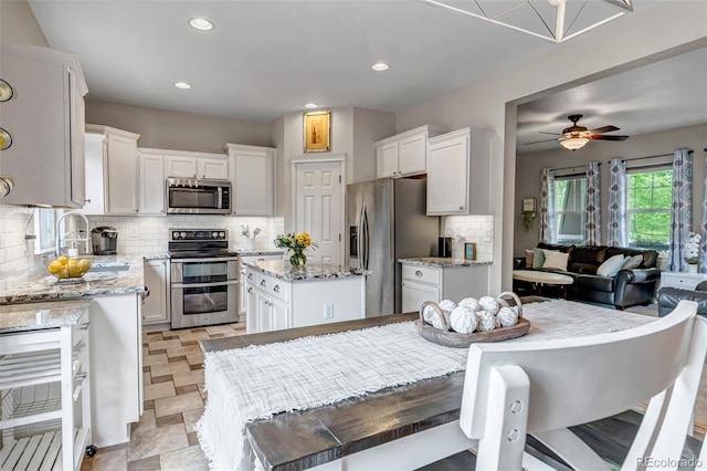 4578 Quandary Peak St, Brighton, CO 80601 - kitchen with appliances with stainless steel finishes, decorative backsplash, a sink, white cabinets, and light stone counters