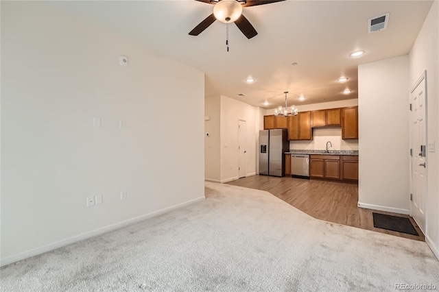 kitchen with brown cabinets, stainless steel appliances, light countertops, light carpet, and a sink