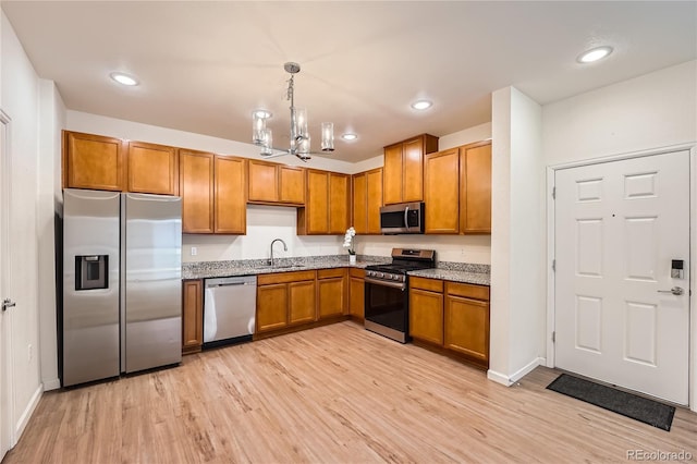 kitchen with a sink, appliances with stainless steel finishes, light wood-type flooring, brown cabinetry, and pendant lighting