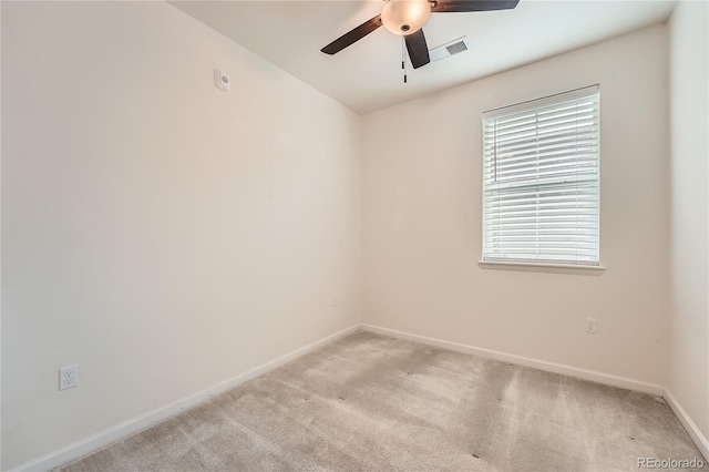 spare room with a ceiling fan, light colored carpet, visible vents, and baseboards