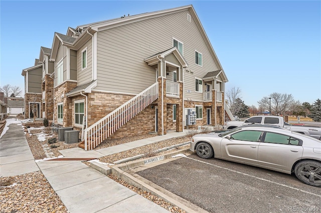 view of side of property featuring central air condition unit, uncovered parking, a residential view, stone siding, and stairs