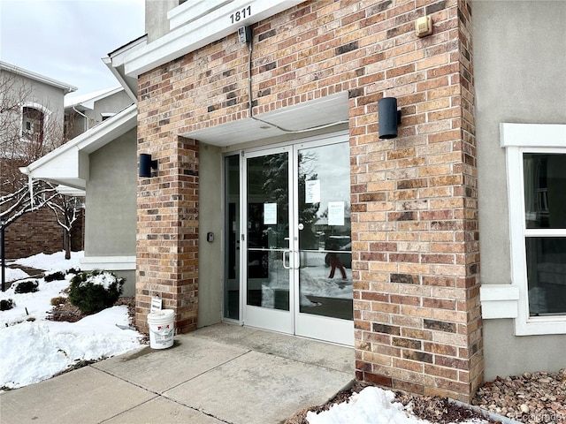 snow covered property entrance featuring brick siding and a patio