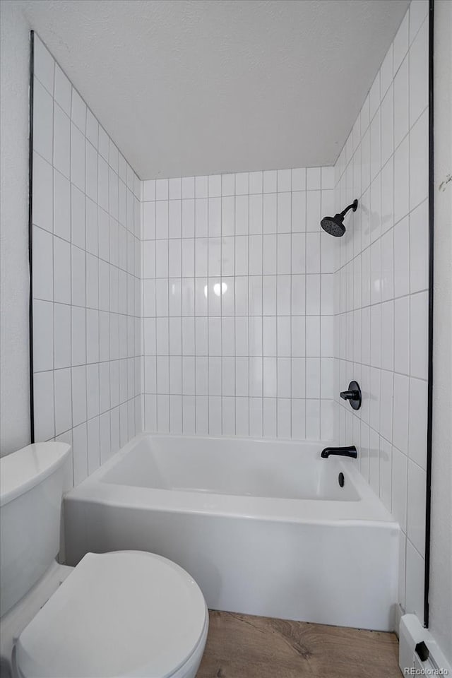 bathroom featuring wood-type flooring, toilet, and tiled shower / bath